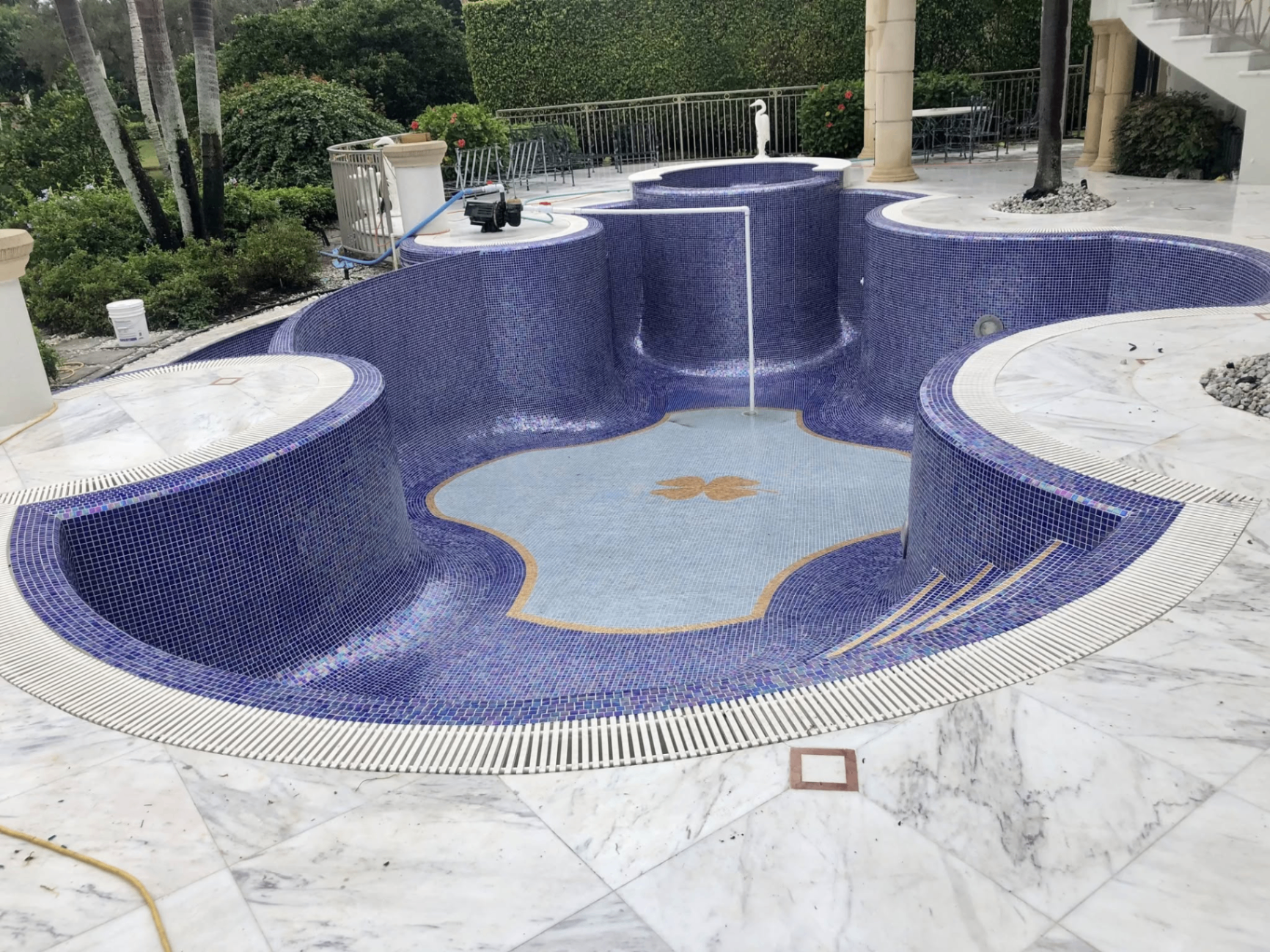 Custom cobalt blue mosaic pool with marble deck and gold medallion inlay